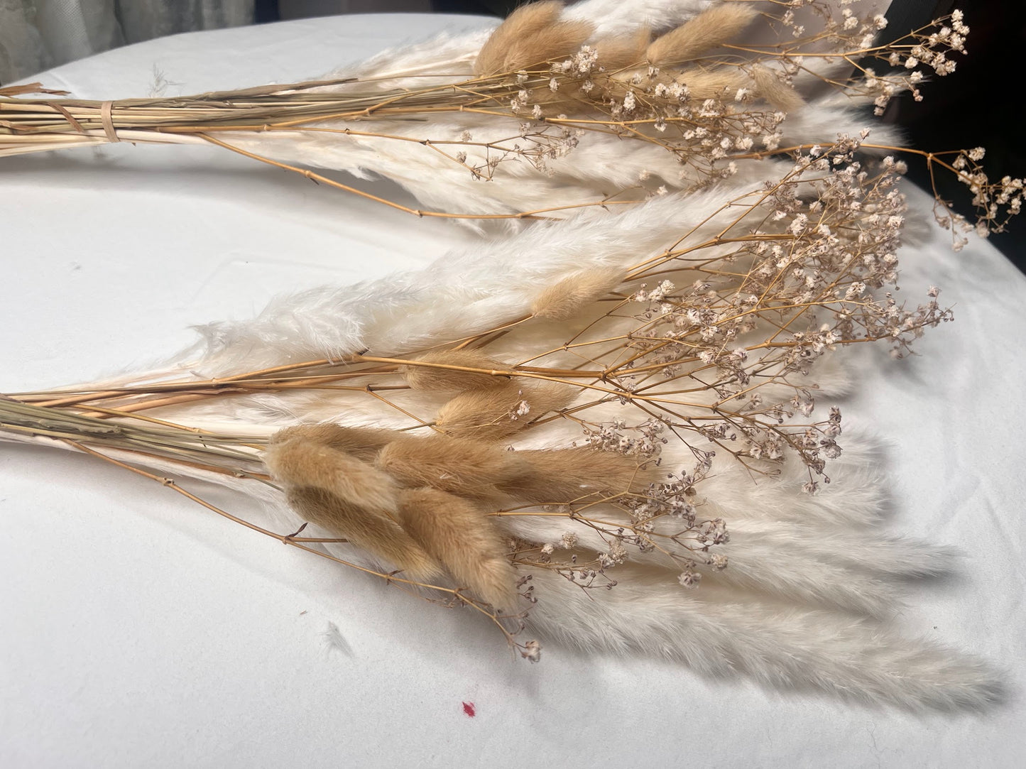 Dried bouquets with baby's breath and small pampas grass and bunny tails on a textured white surface