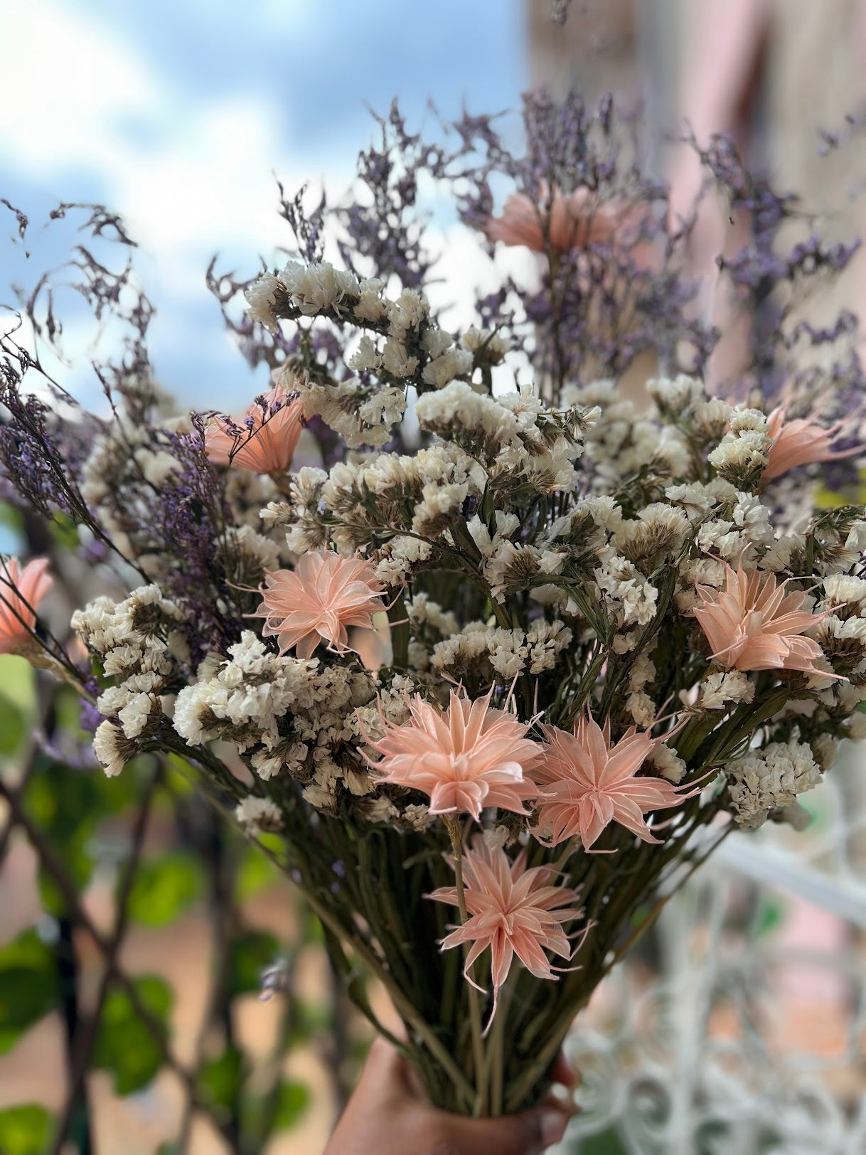 Bouquet of dried flowers with purple, pink and white elements held by a hand against a blurred natural background.