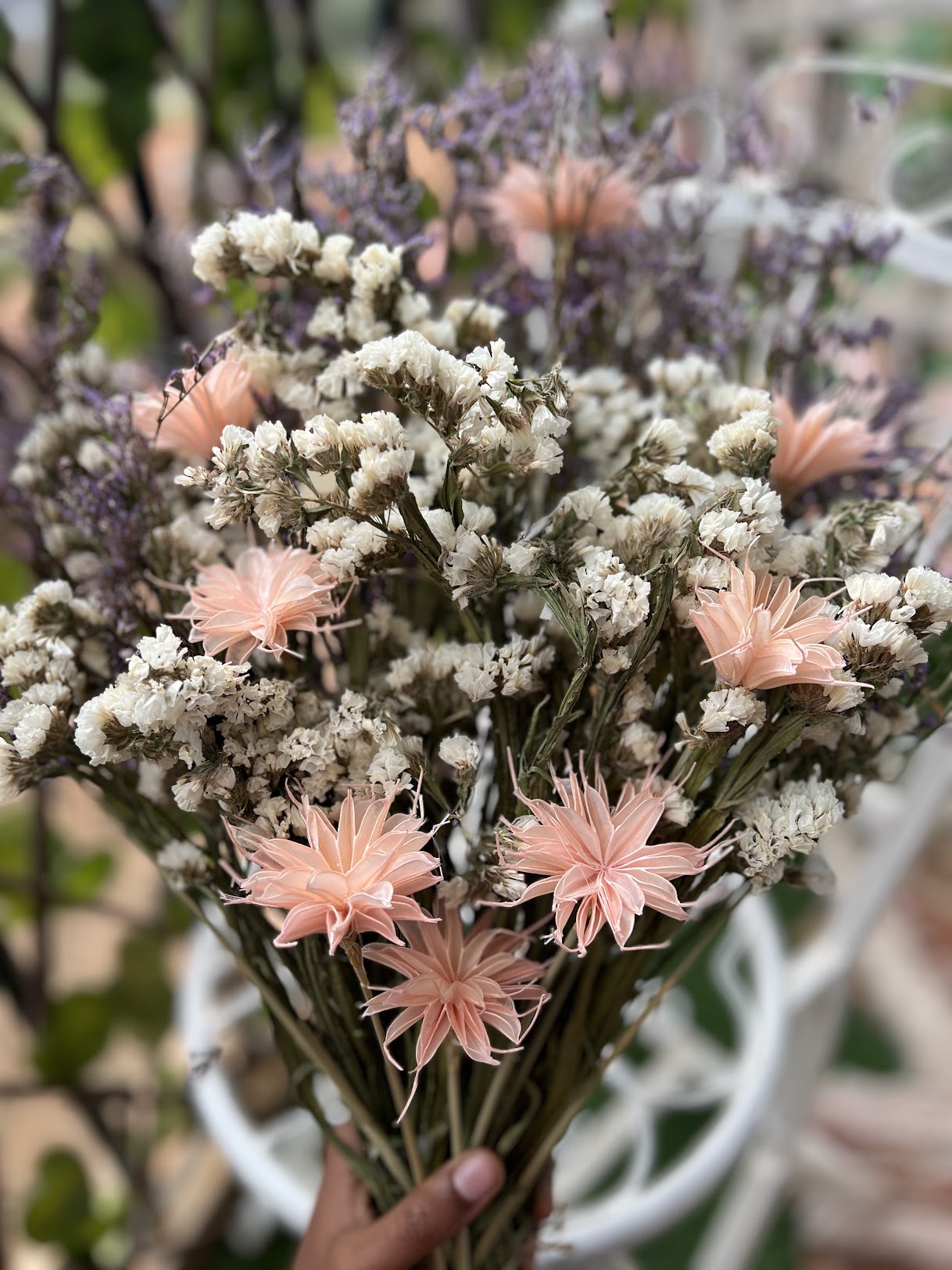 Bouquet of pirple, pink and white flowers held by a hand with a blurred background