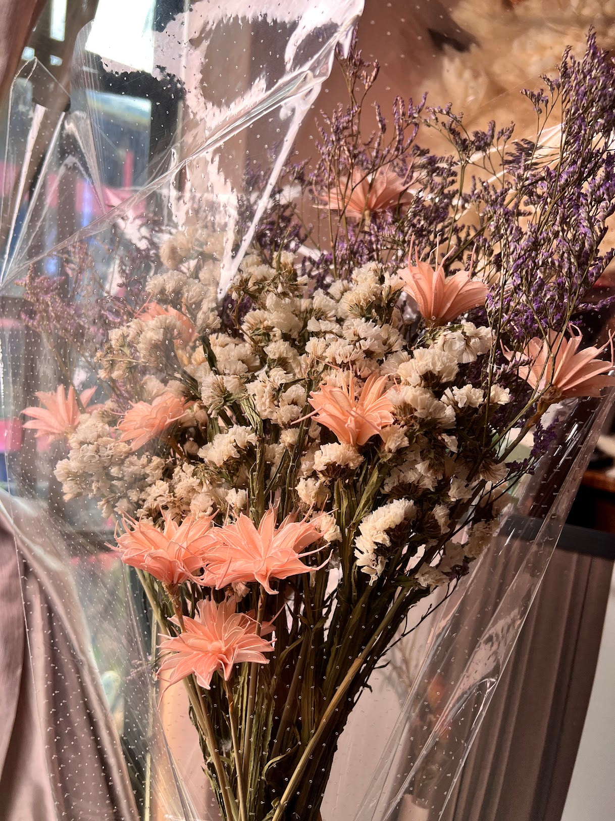 Bouquet of dried flowers with purple, pink and white blooms in clear plastic wrap.