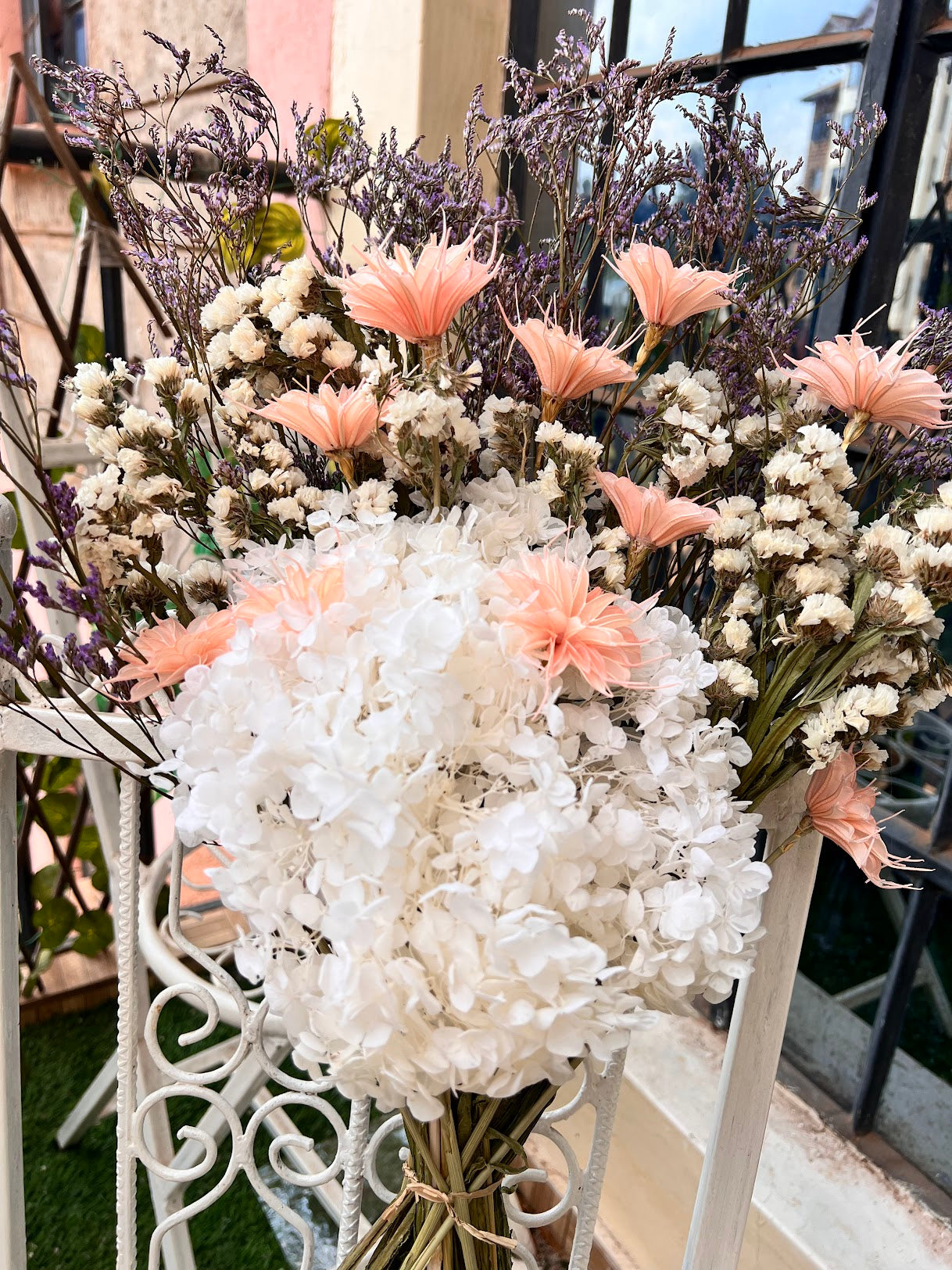Bouquet of flowers with white, pink, and purple elements of dried flowers on a decorative stand.