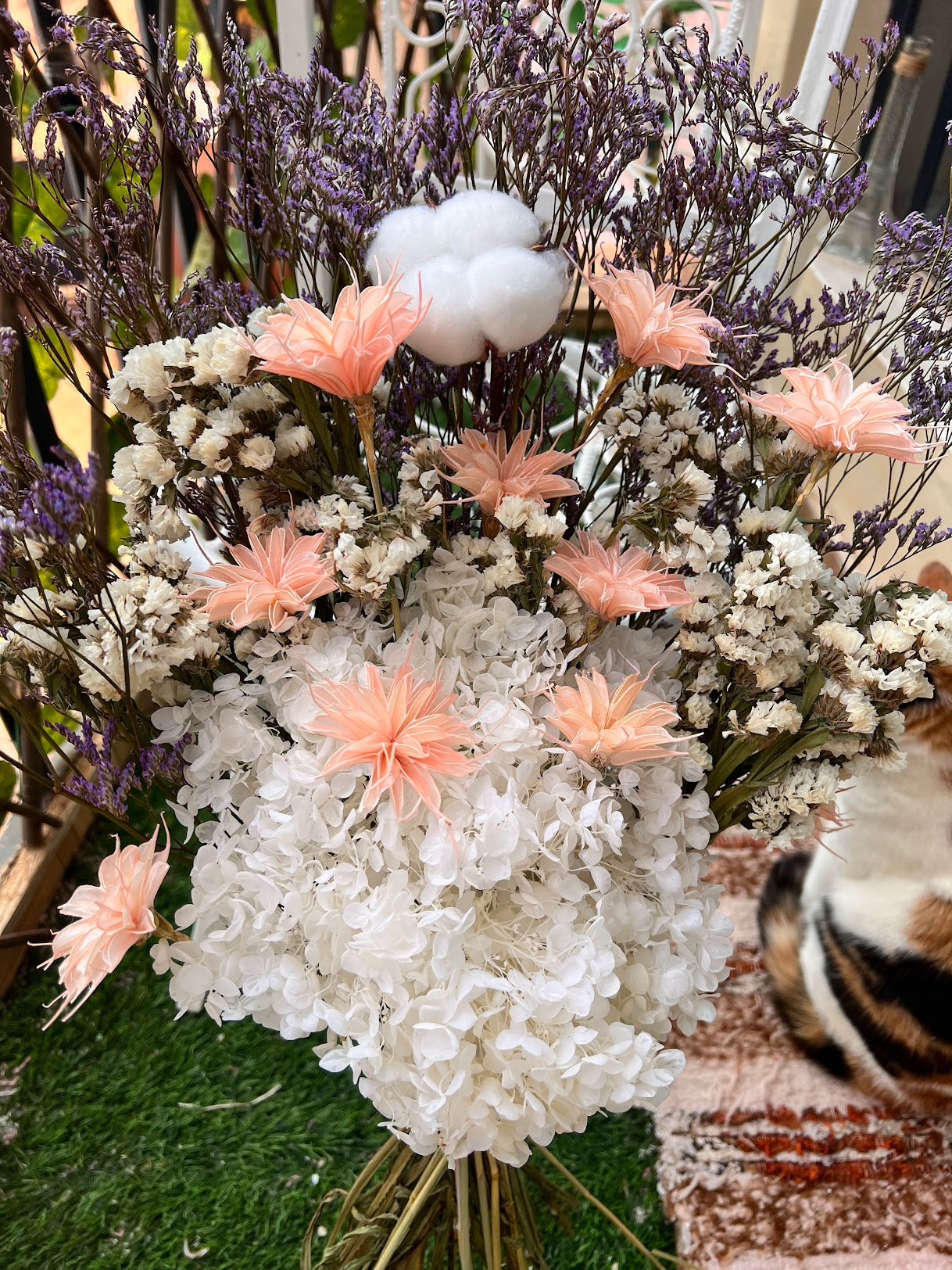 Bouquet of flowers with white and pink preserved and dried flowers, cotton, and dried elements on a textured surface.