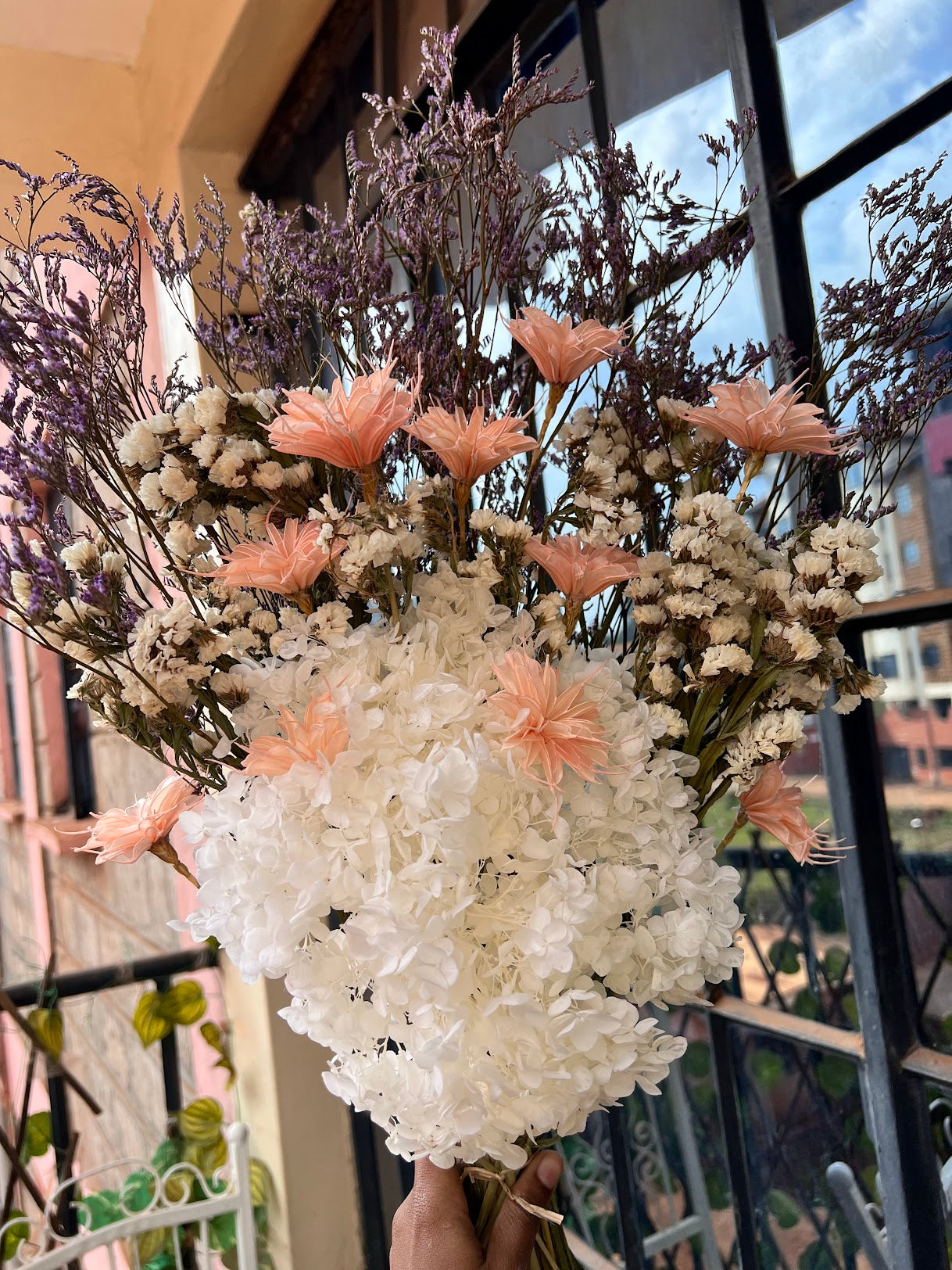 Bouquet of white and pink dried and preserved flowers held by a hand outdoors.