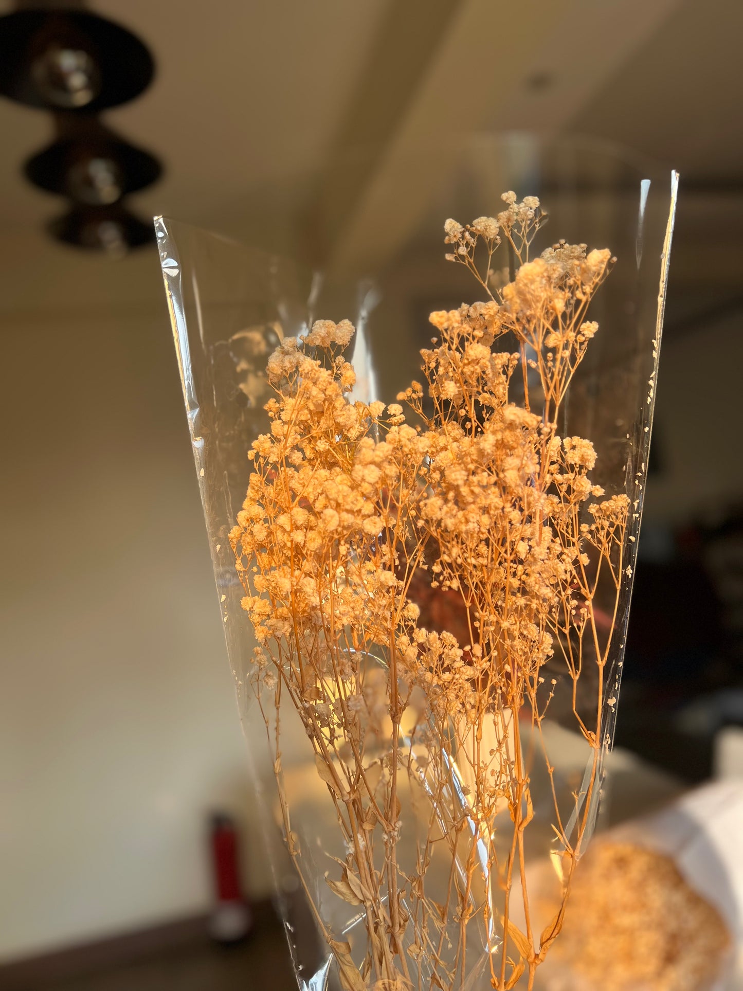 A bouquet of dried baby's breath flowers from kenyan lady fleur nairobi flower shop wrapped in clear cellophane packaging, held up against a softly blurred indoor background.