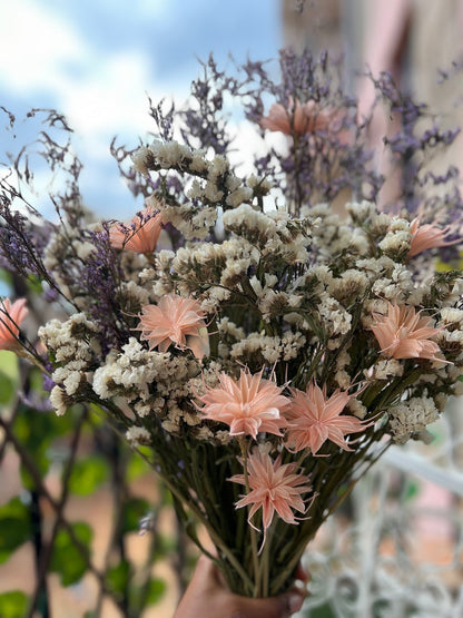 Bouquet of dried flowers with purple, pink and white elements held by a hand against a blurred natural background.