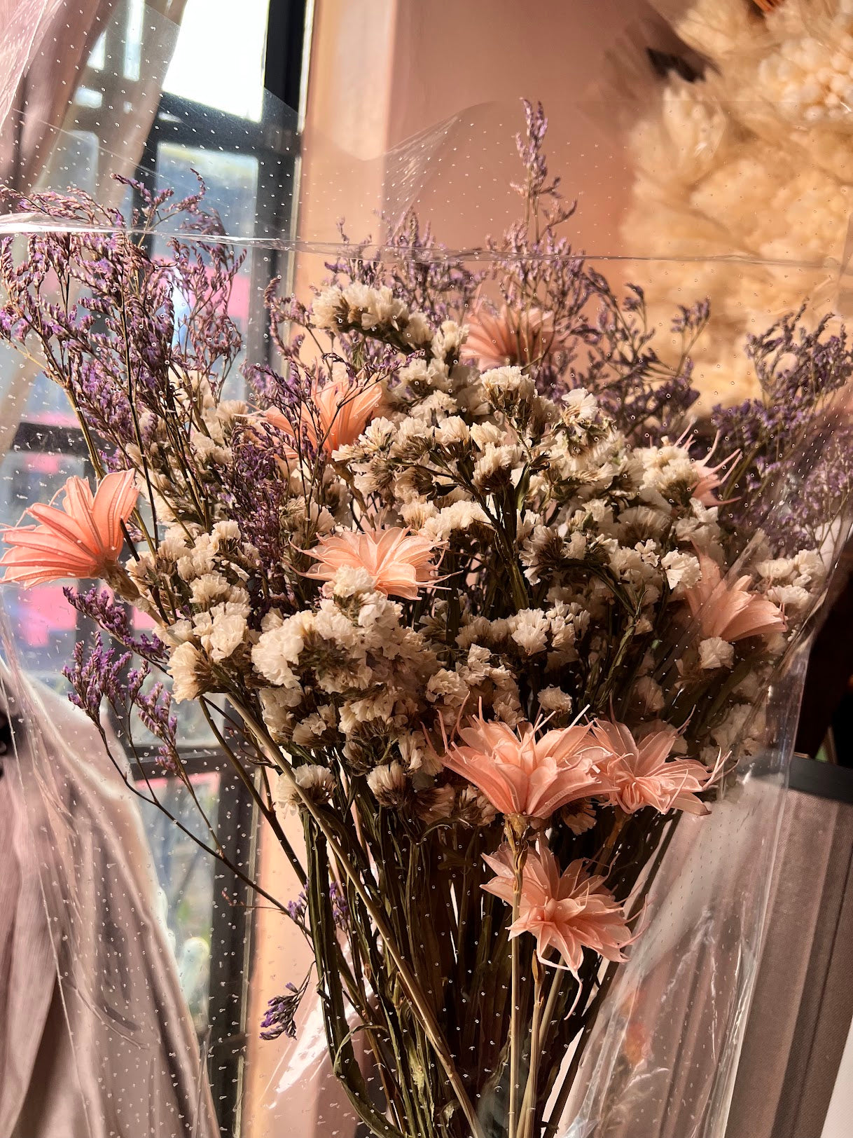 Bouquet of dried flowers with pink and beige tones in front of a blurred indoor background.