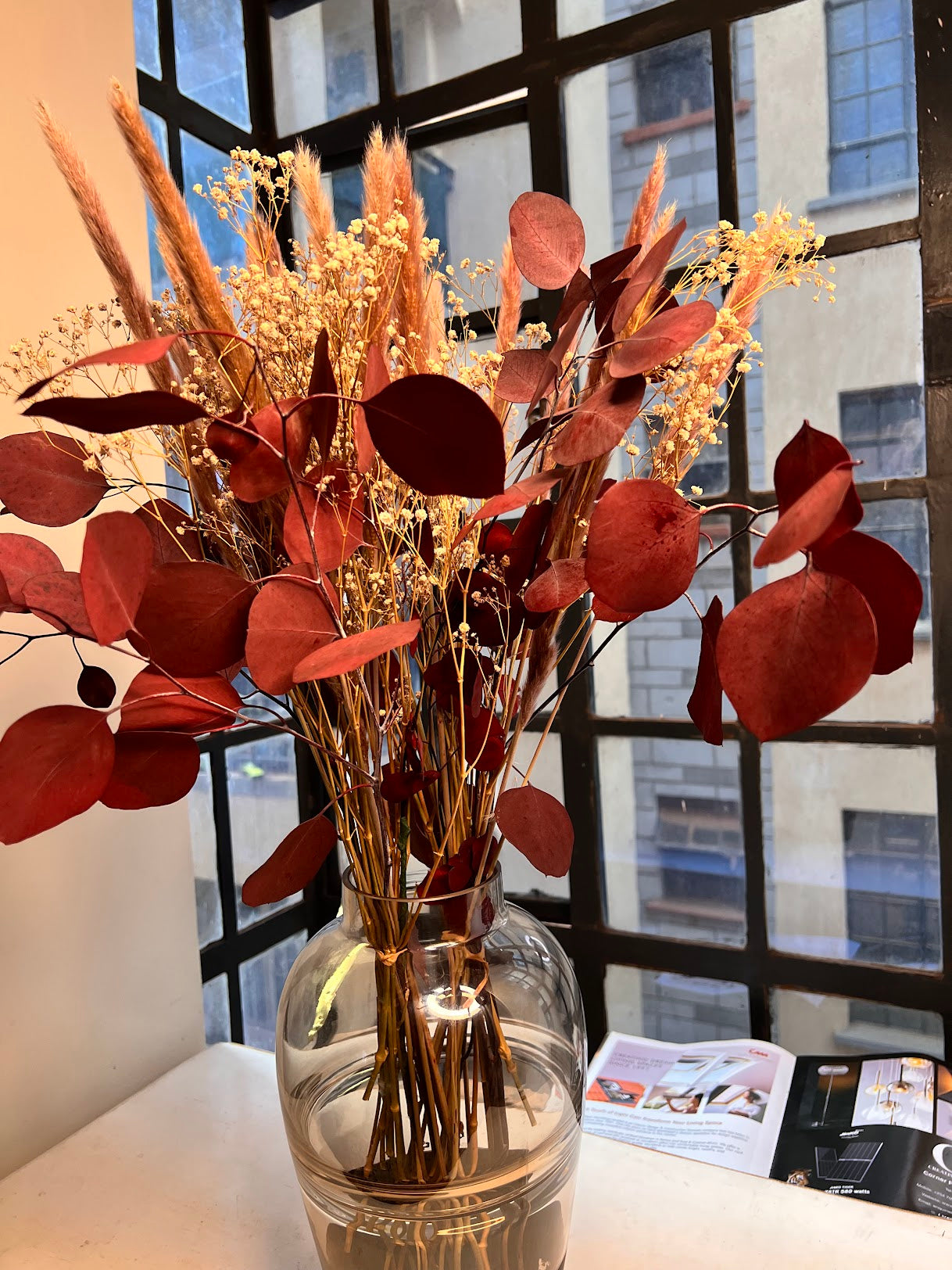 Decorative vase with dried flowers in front of a window with a cityscape view