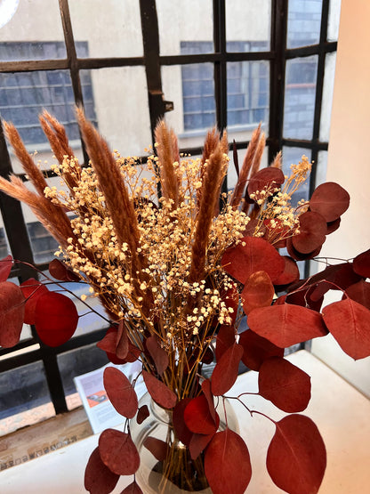 Bouquet of dried grasses and red leaves in a vase with a window in the background
