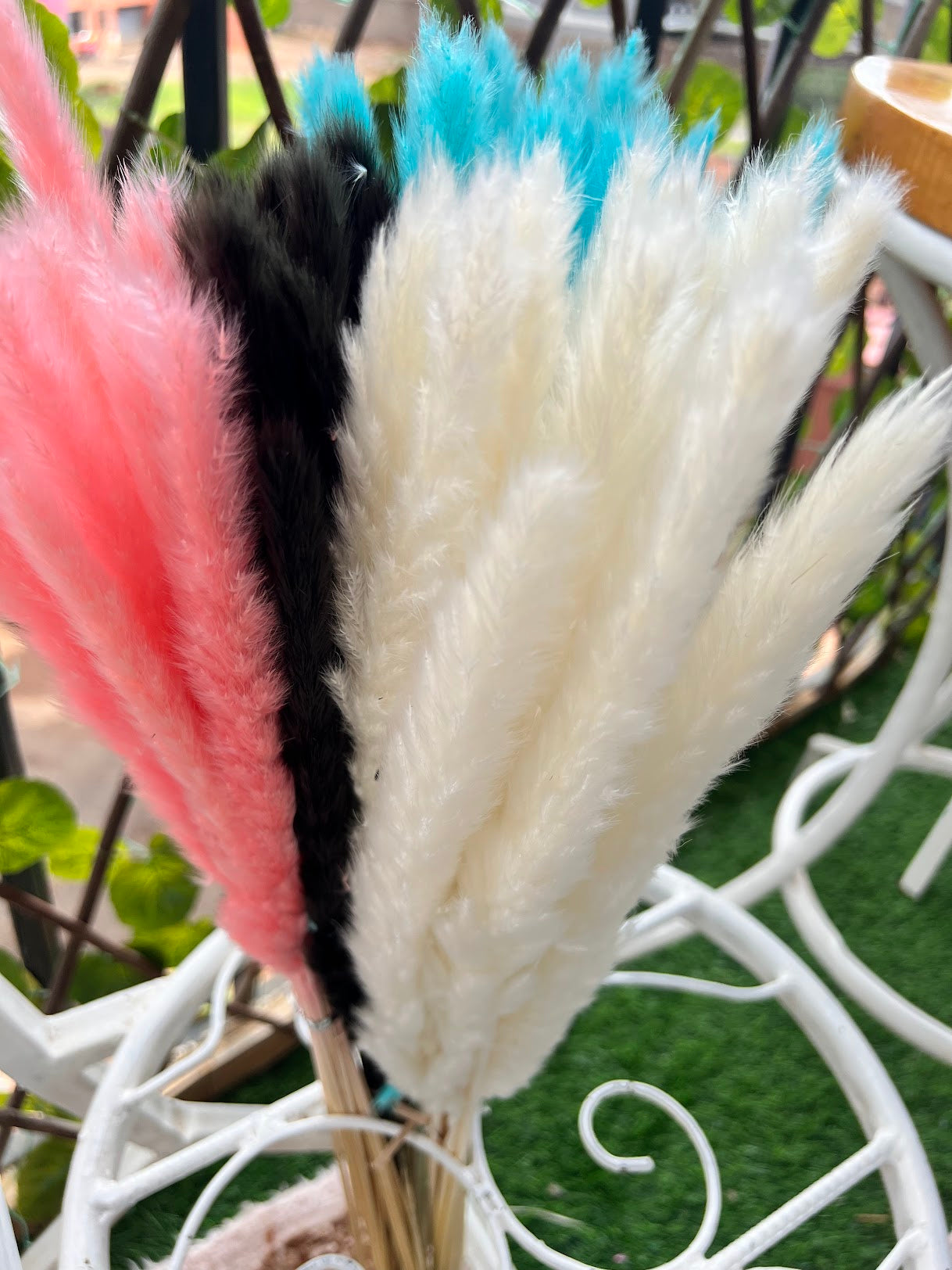 Decorative arrangement of dried small pampas grass with pink, blue, and white colors on a blurred outdoor background.