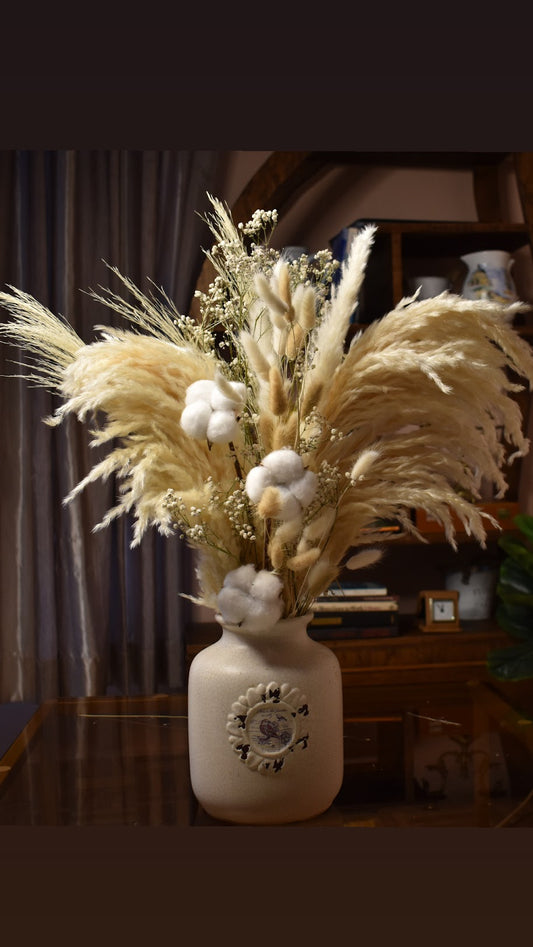 Decorative vase with dried pampas grass, other dried flowers and cotton on a wooden surface