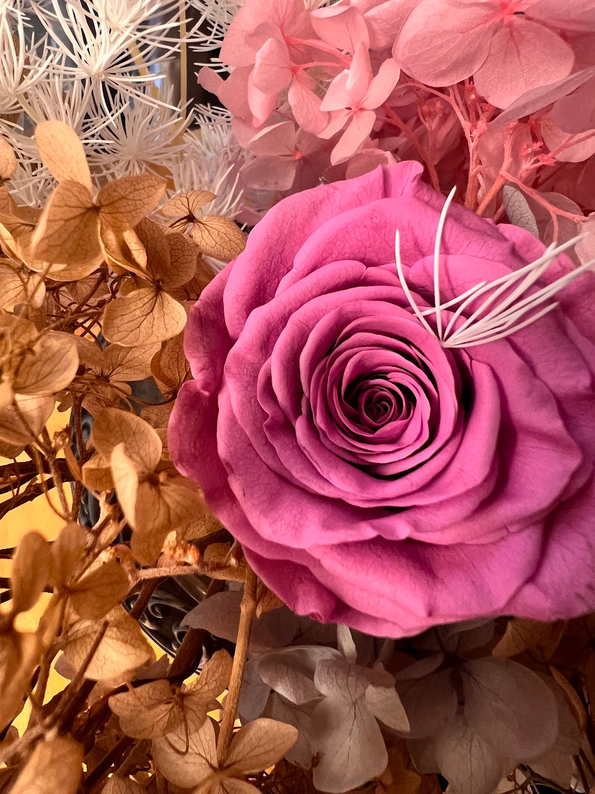 Close-up of a pink rose surrounded by dried flowers and leaves